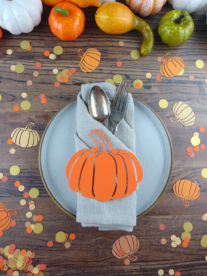 Autumn table set up featuring papercut pumpkin place decoration and orange pumpkin confetti scattered on wooden table