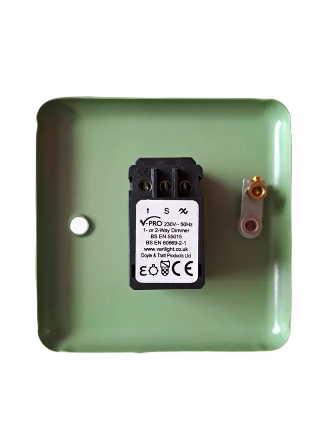 The back of a green steel metal epoxy coated light switch plate, there is a black rectangle LED dimmer switch module in the centre of the switch plate, the module has three round holes at it’s base for wires and a white label with V Pro, 230v – 50Hz 1 or 2 way Dimmer, BS EN 55015, BS EN 60669 – 2- 1 www.varilight.co.uk, Doyle & Tratt products Ltd written one it, there are two screw holes in the light switch, the hole on the left also has an earthing screw on it.