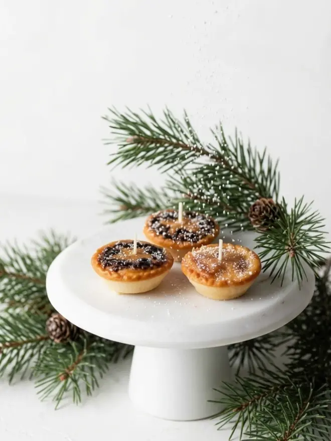 The mince pie candle. three candles shaped like mince pies on a white cake stand.
