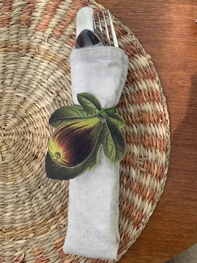 Botanical fig napkin ring tie around a linen napkin and cutlery bundle on a mid century place setting