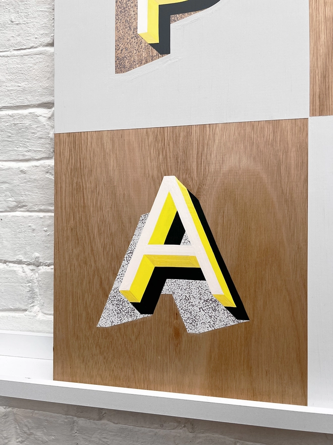 Close up of letter A from PLAY hand painted sign in neon yellow, lilac and grey, against a white brick wall, straight on. 