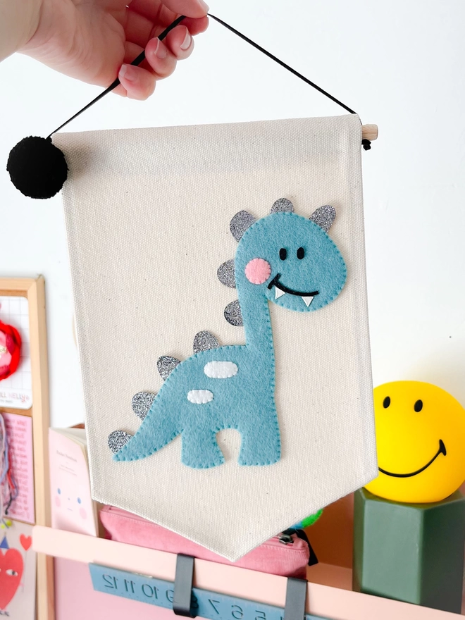 Blue dinosaur on a cream fabric banner being held up against wall