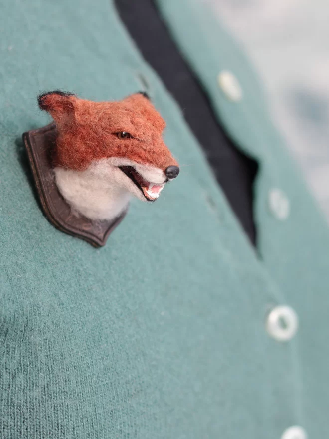 A miniature snarling fox head on a green cardigan