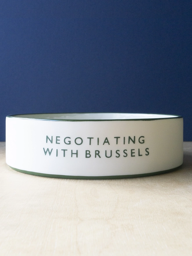 Ceramic porcelain dish with Negotiating with Brussels written on the side. A white Christmas serving dish with green rim.