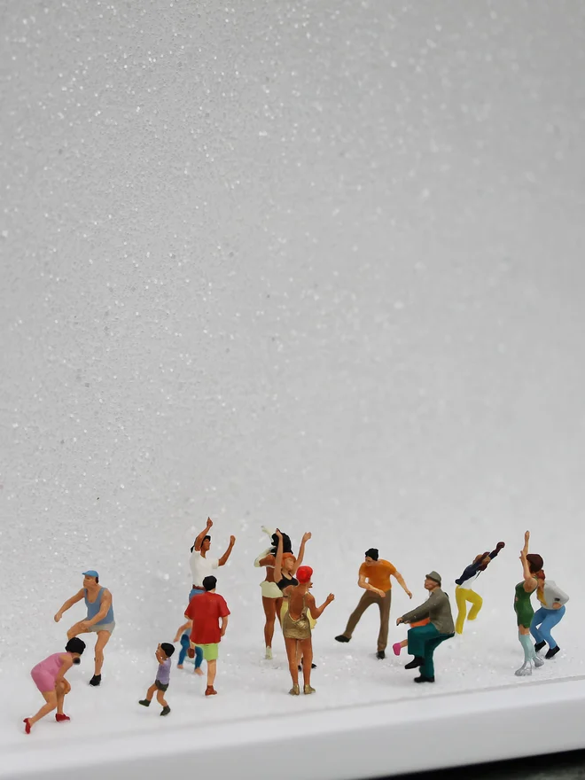 Miniature scene in an artbox showing about 15 tiny people dancing their hearts out, set against a sparkling white backdrop (close up). 