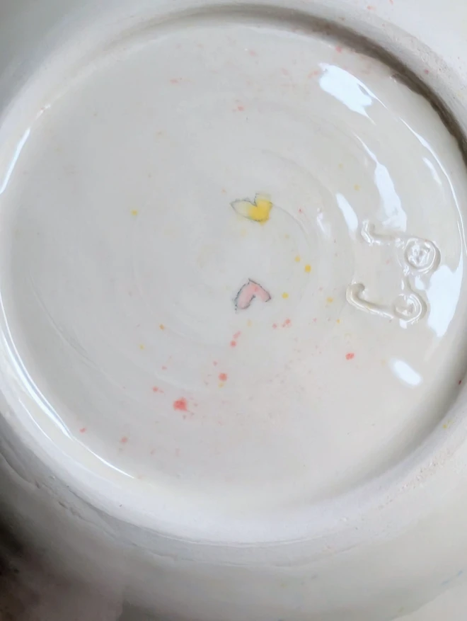 the base of a ceramic glazed bowl showing a pink and yellow heart with splatters of paint