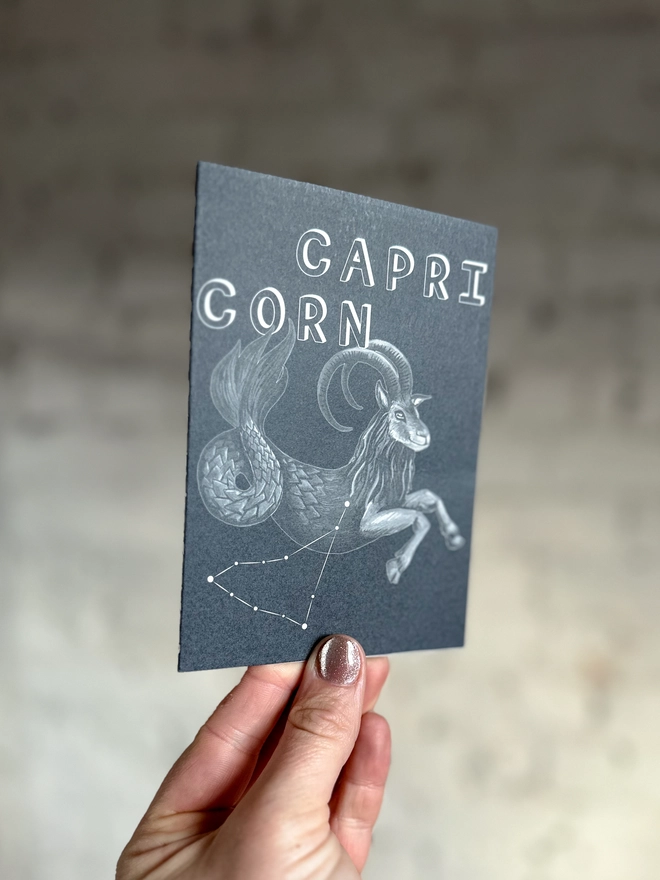 a greetings card featuring a greyscale illustration of a zodiac style sea goat with the text “CAPRICORN”