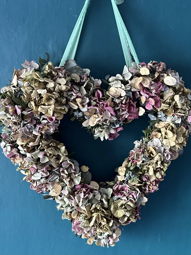 dried violet hydrangea heart shaped wreath. a heart shaped dried flower wreath hung up on a blue wall.