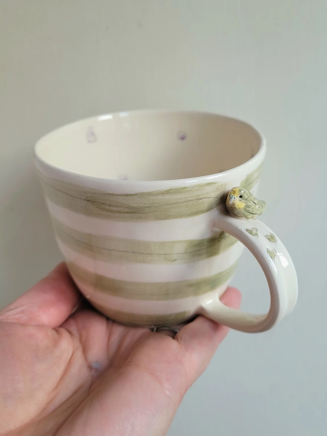 Green striped ceramic cup withca tiny modelled budgie bird on the handle