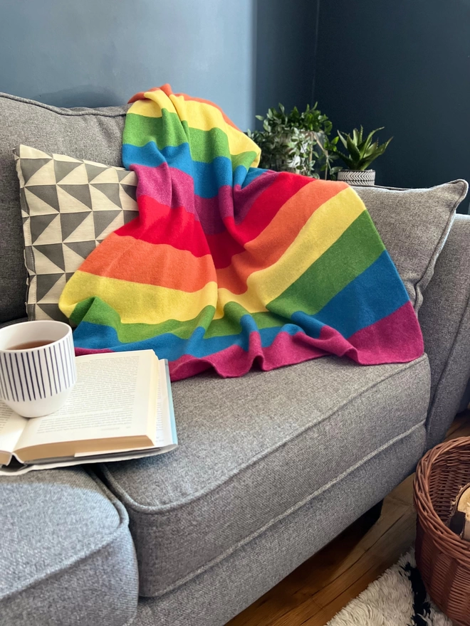 Knitted rainbow blanket shown draped over the edge of a sofa