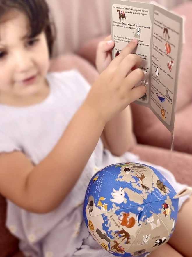 Girl holding first globe soft toy and the guide that comes with it. She is pointing at a Snow Leopard on the guide