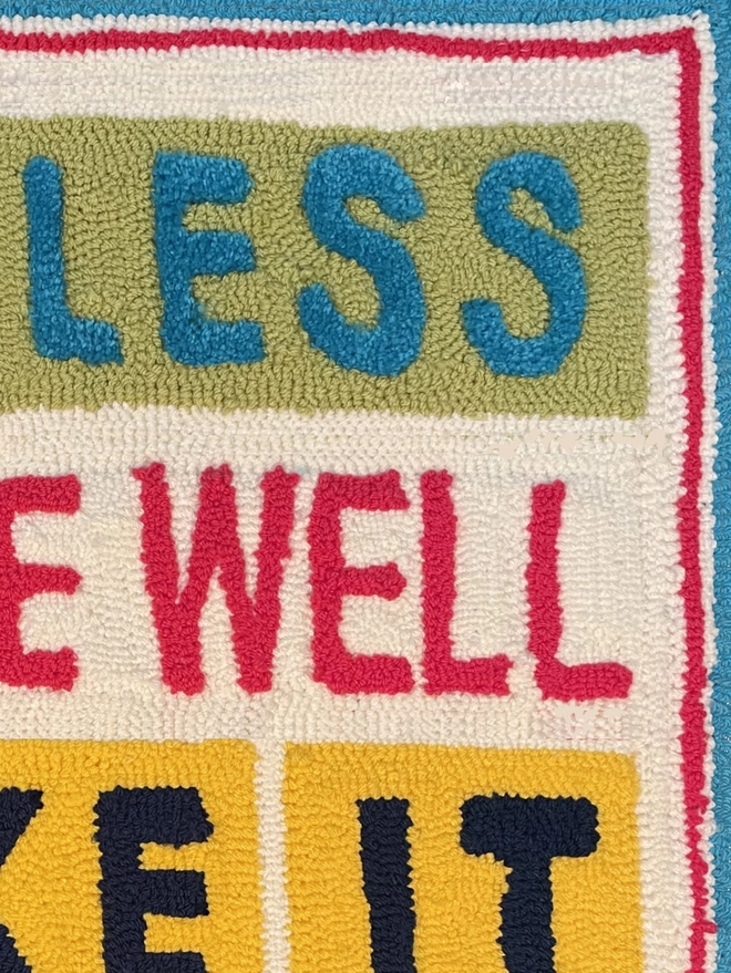 Close up of "less", "well" and it, bright tufted wool on square coloured block backgrounds