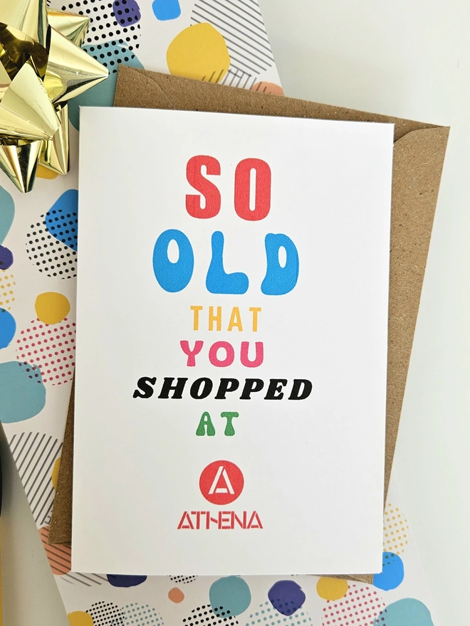 A photograph of the front of a humorous A6 greeting card illustrated using brightly coloured text and the retro shop logo. The text says so old you shopped at Athena.
