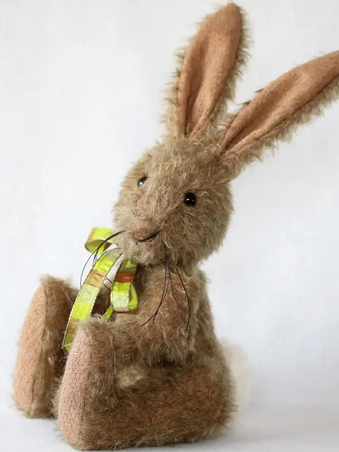 Handmade brown stuffed rabbit with long ears and a green ribbon bow sitting upright against a plain background.