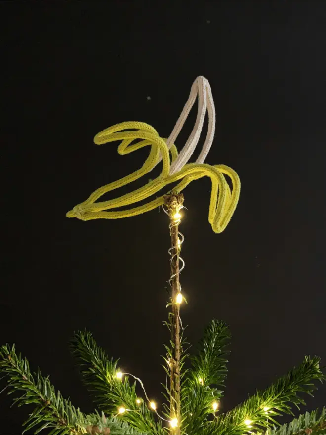 Xmas tree topped with a string and wire peeled banana tree topper against a black background