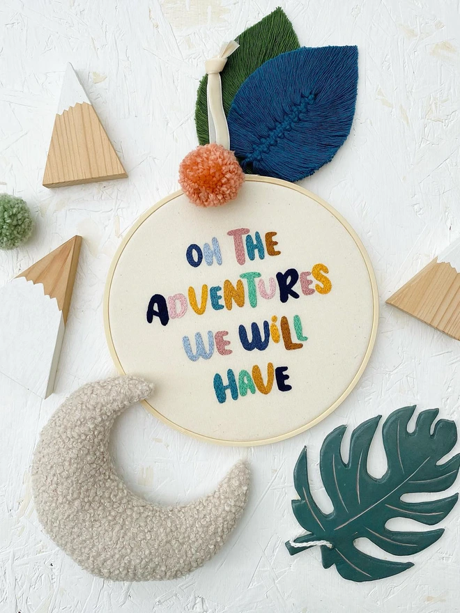 custom phrase embroidered hoop. cotton hoop embroidered with 'oh the adventures we will have' in colourful letttering.