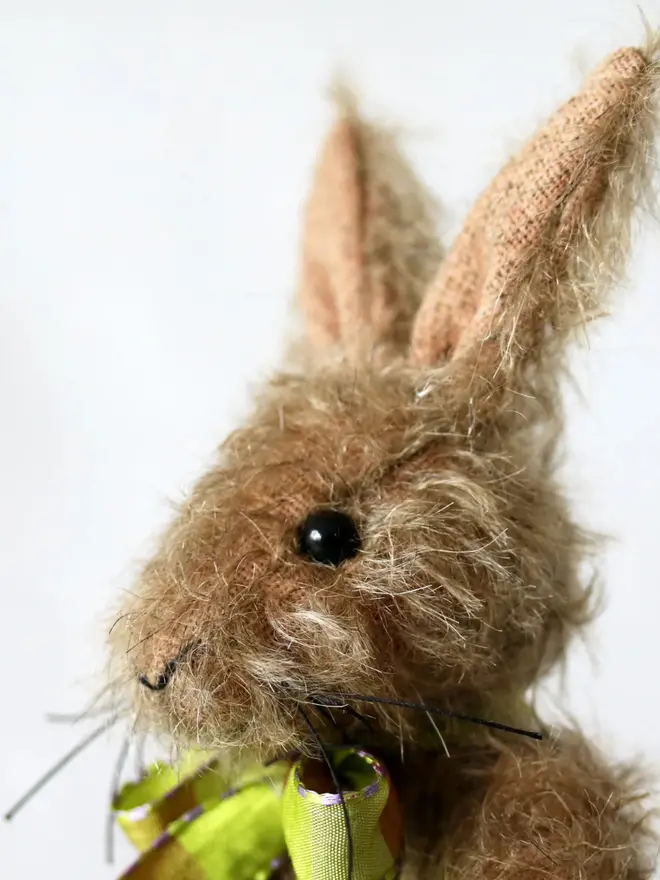 Handmade brown stuffed rabbit with long ears and a green ribbon bow sitting upright against a plain background.