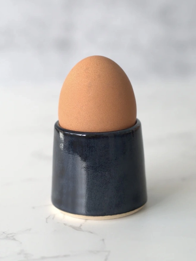 Classic Handmade Egg Cup, a ceramic egg cup sitting on a plain surface against a grey backdrop. 
