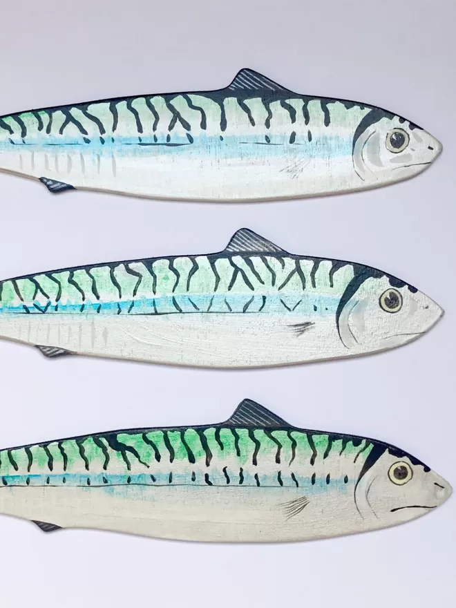 3 wooden mackerels hanging on a white wall facing the same direction