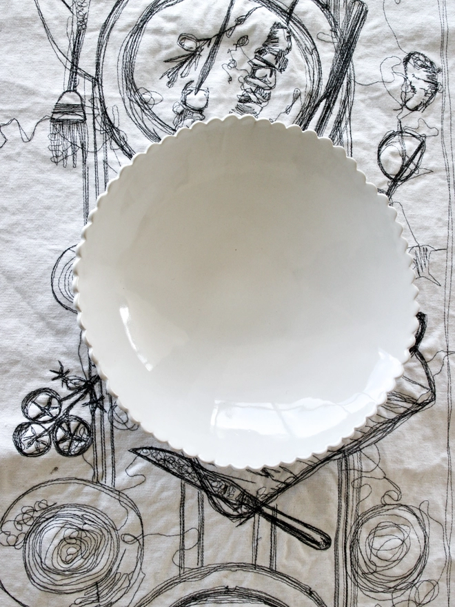 white scalloped edge serving or salad bowl on a white embroidered tablecloth