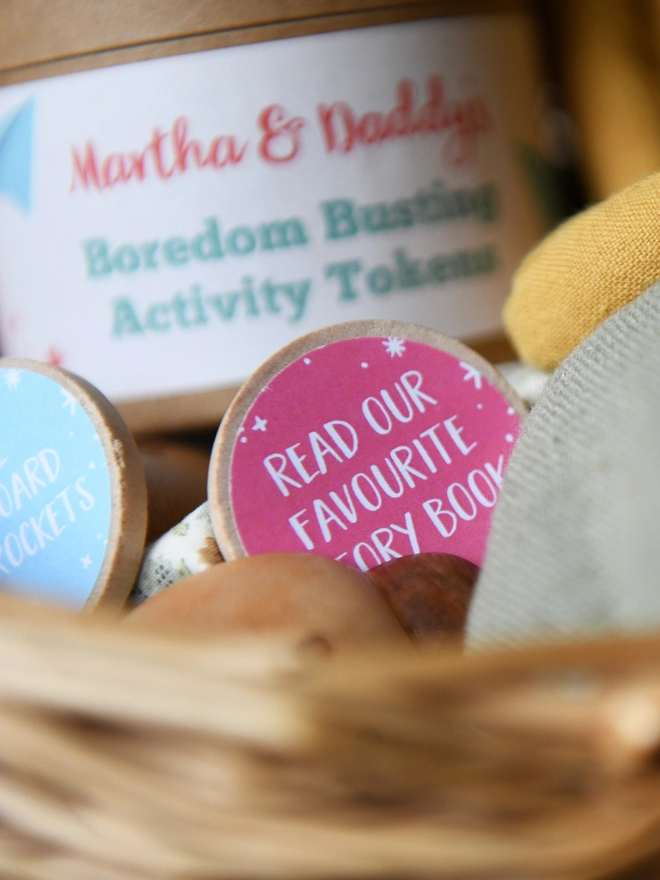 A wooden token with a pink label and the words 'Read our favourite story book' printed on, rests in a wicker basket.