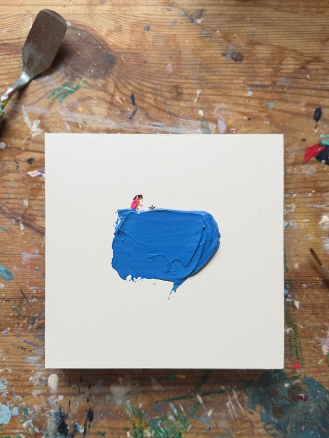 'Yesterdays News Again' Art Piece. Art piece of little girl floating a newspaper boat in blue paint representing a water puddle.