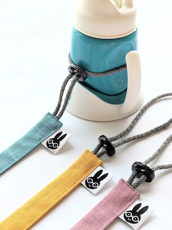 Handmade linen toy strap with grey string and a toggle attached to a baby drinking bottle.