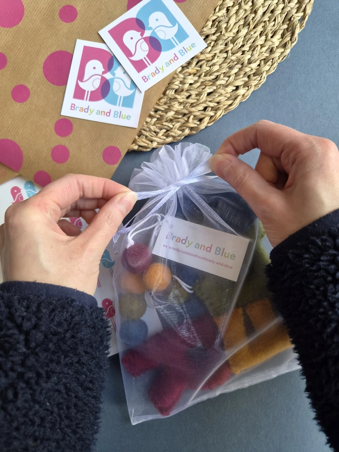 A garland in an organza bag, with some hands tying a bow in the ribbon.