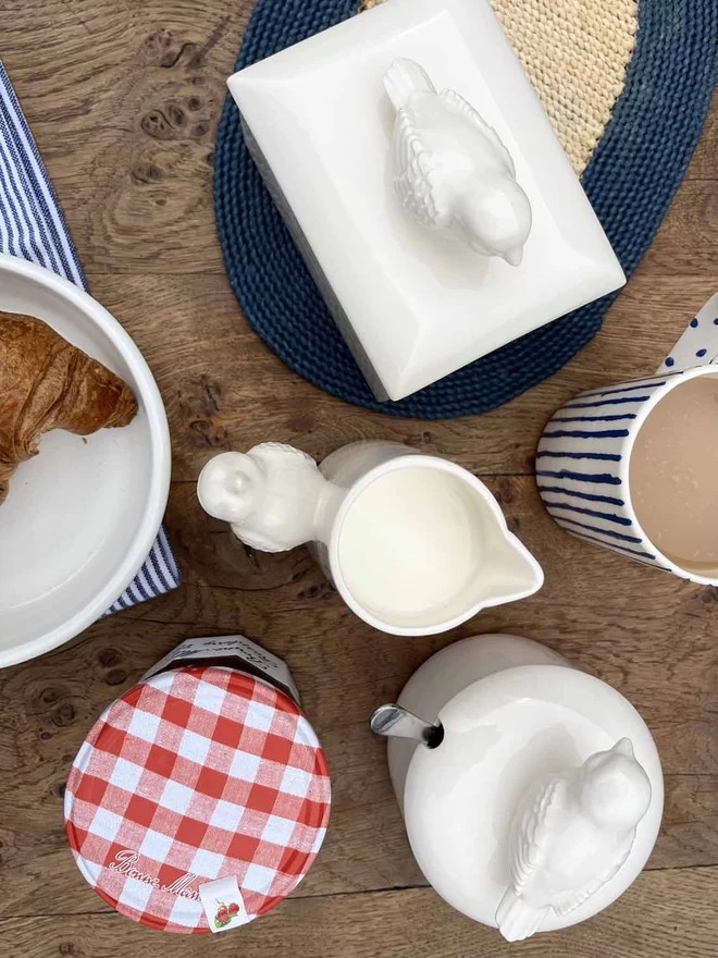 An above view of handmade ceramic sugar pot, butter dish and jug all with matching bird handles.