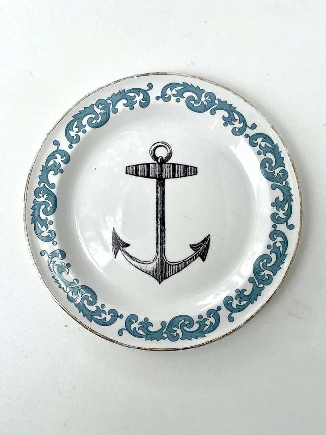 vintage plate with an ornate border, with a printed vintage illustration of an ship's anchor in the middle 