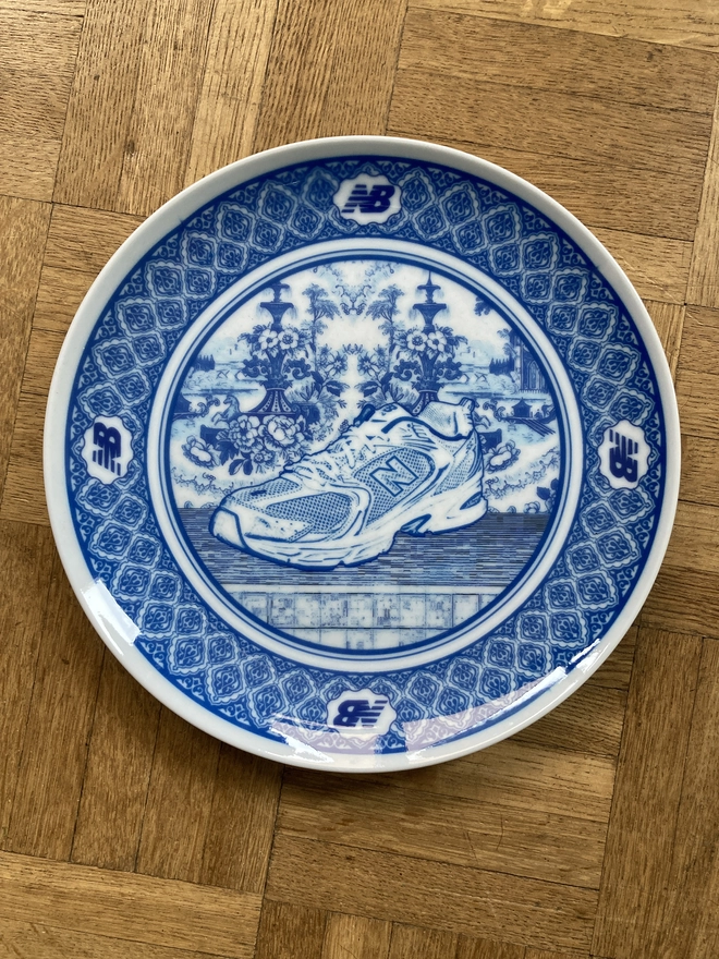detail of plate showing the New Balance logo. The plate is blue and white in a Delft style featuring an illustration of a New Balance trainer in the centre
