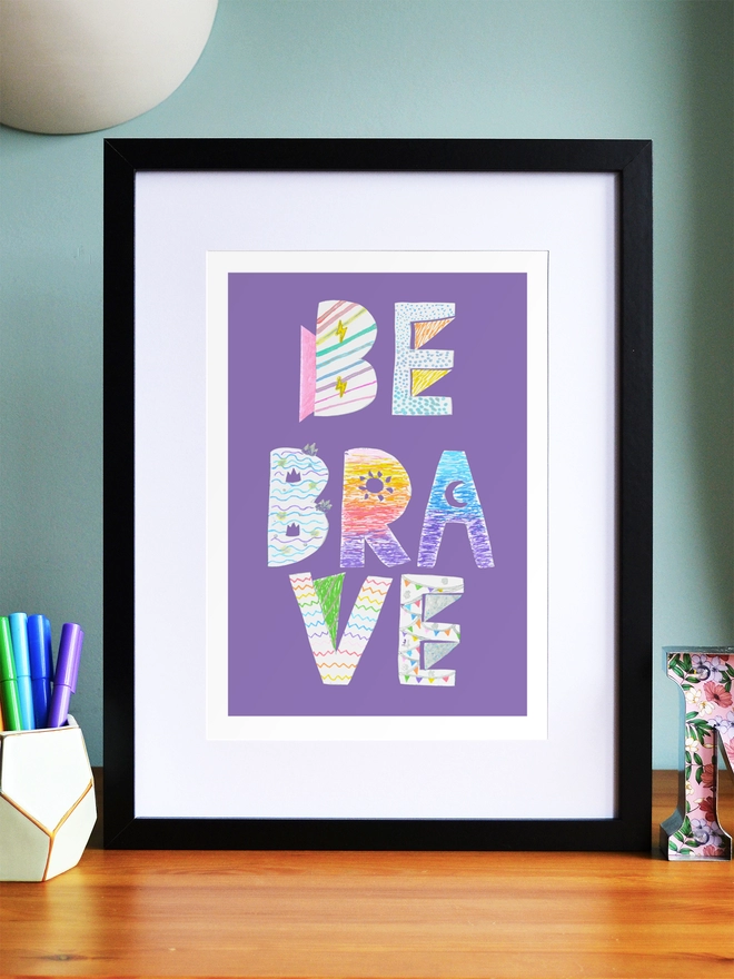 Art print saying 'Be brave' in a black frame in a child's room