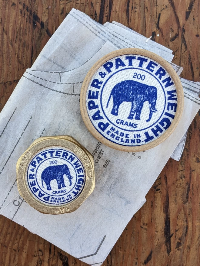 Blue elephant brass pattern & paper weight with lying on a sewing pattern next to its box