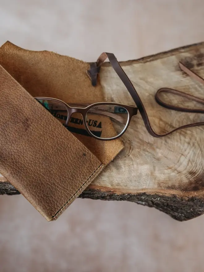 hand stitched leather pouch. a brown leather pouch on a cream cow hide background with a brown strap.