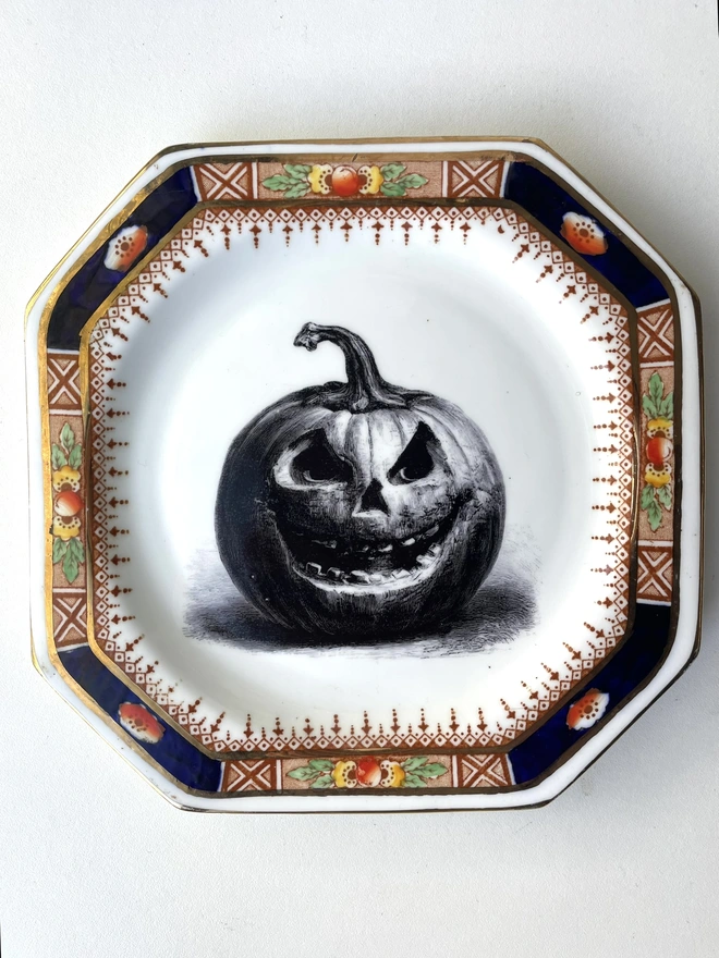 vintage plate with an ornate border, with a printed vintage illustration of a creepy pumpkin in the middle 
