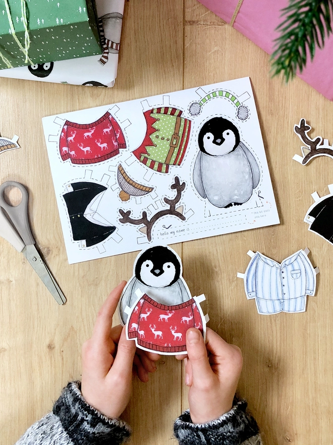 A child is playing with a dress up penguin paper doll that has been cut from a Christmas greetings card.