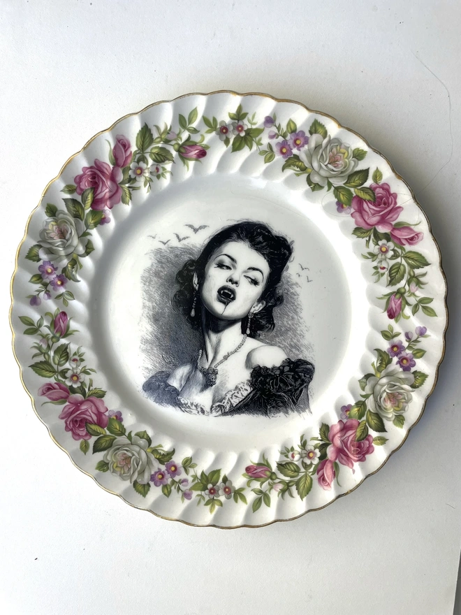 A vampire with bats behind her, the image is victorian in black and white and is printed directly onto an ornate vintage plate