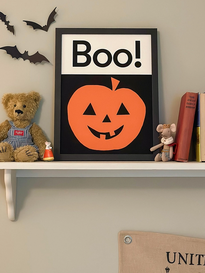 Pumpkin wall print on shelf beside teddy bear and books
