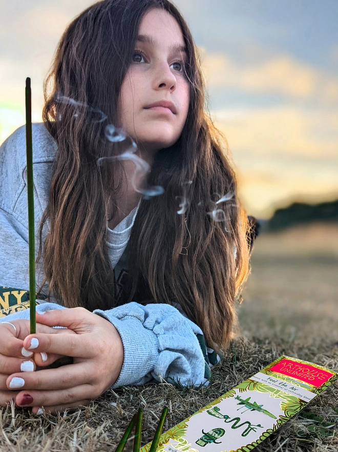 girl in a field feel the air well being charity incense sticks with gold & green illustrations
