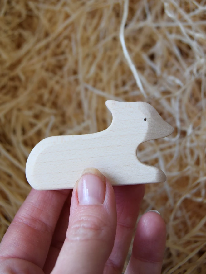 wooden lamb toy white lying down toy held in hand above woodwool