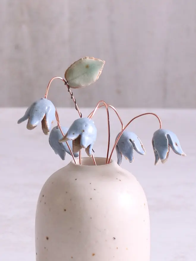 Close up of ceramic bluebell drop flowers and leaf in small white vase