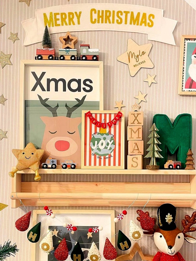 illustrated reindeer wall print with the word Xmas sitting against a wall surrounded by christmas toys