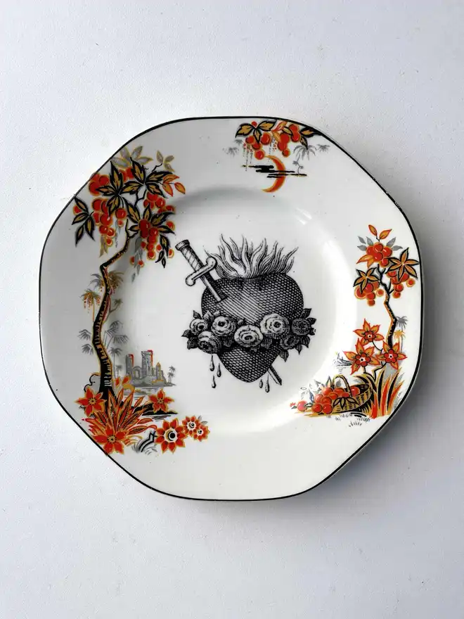a vintage plate with an ornate border, the centre is white and printed on that is a black illustration of a sacred heart