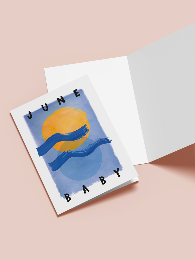 june baby illustrated card. a blue card with illustrated sun, moon and waves in the centre.