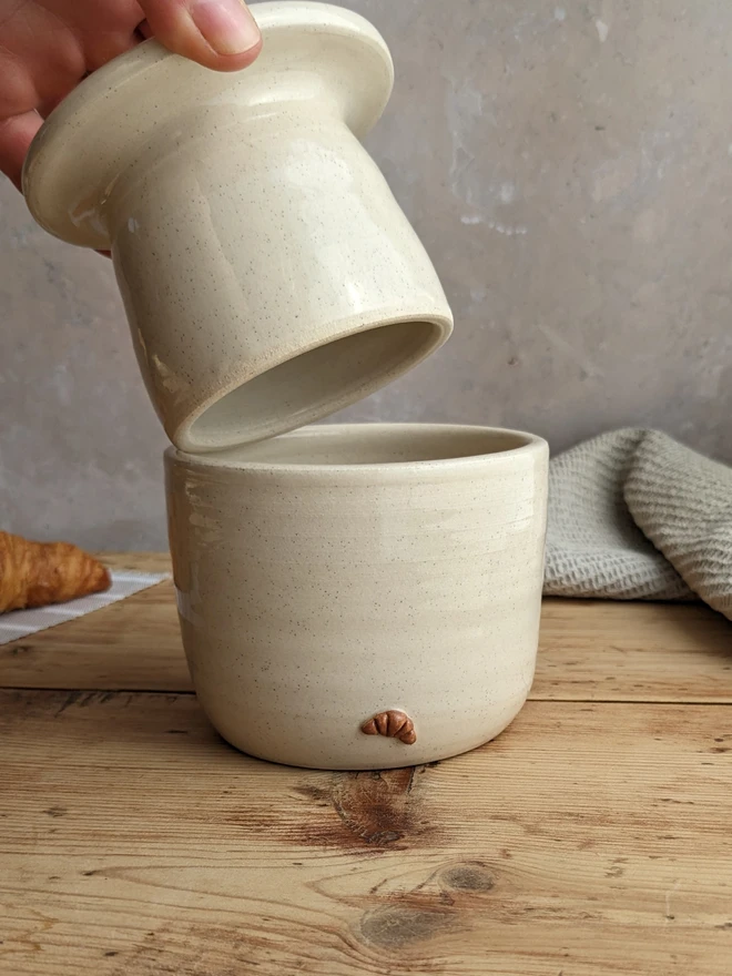 Croissant Butter Crock in vanialla glaze with a small croissant design on the front, set against a grey background.