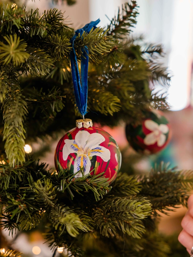 Hand painted floral ceramic christmas bauble dark pink background with Algerian winter iris flowers.