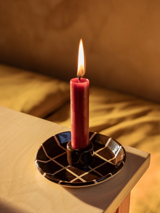 Ceramic Patterned Candlestick Holder, a colourful candlestick holder sitting on a table stop surface. It is accompanied by a lit candle. 