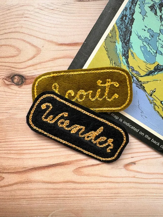 Two custom chain stitch embroidered patches in black and willow laying on a vintage map