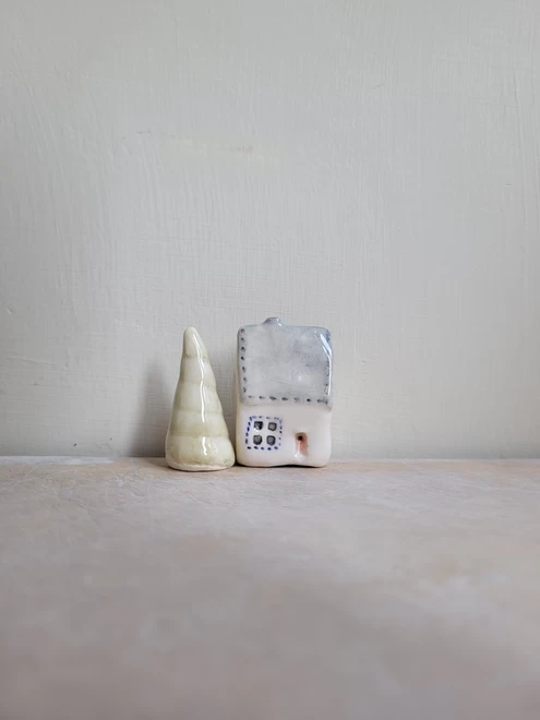 Clay glazed house with a grey roof and etched in windows doors with a grey roof and red front door next to a pale green ceramic tree