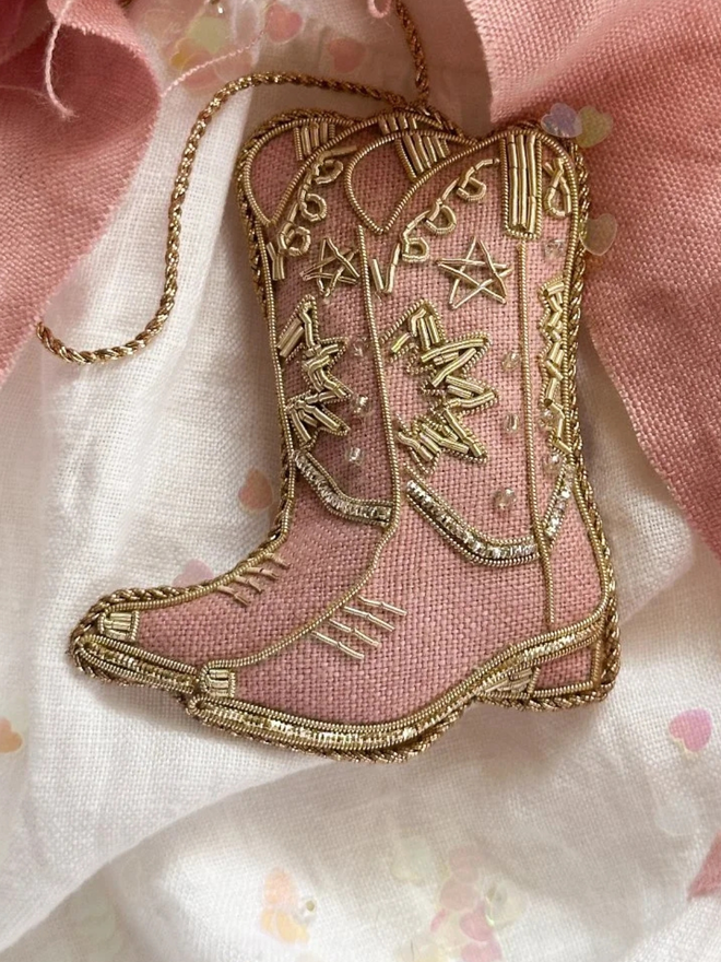 embroidered linen pink cowboy boots decorations. cowboy boot hanging ornaments with gold detailing photographed on white sheet.